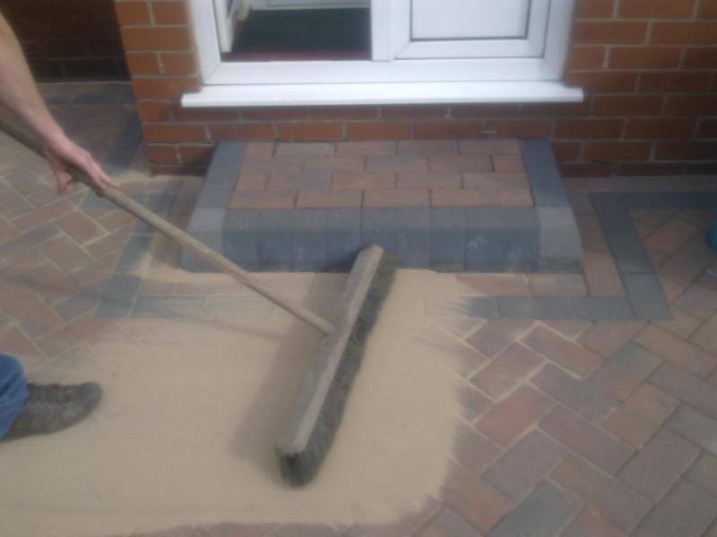 Kiln dried sand being brushed into the joints of newly laid block paving
