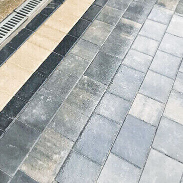 Close up of grey and charcoal block paving meeting a buff soldier course beside a channel drain